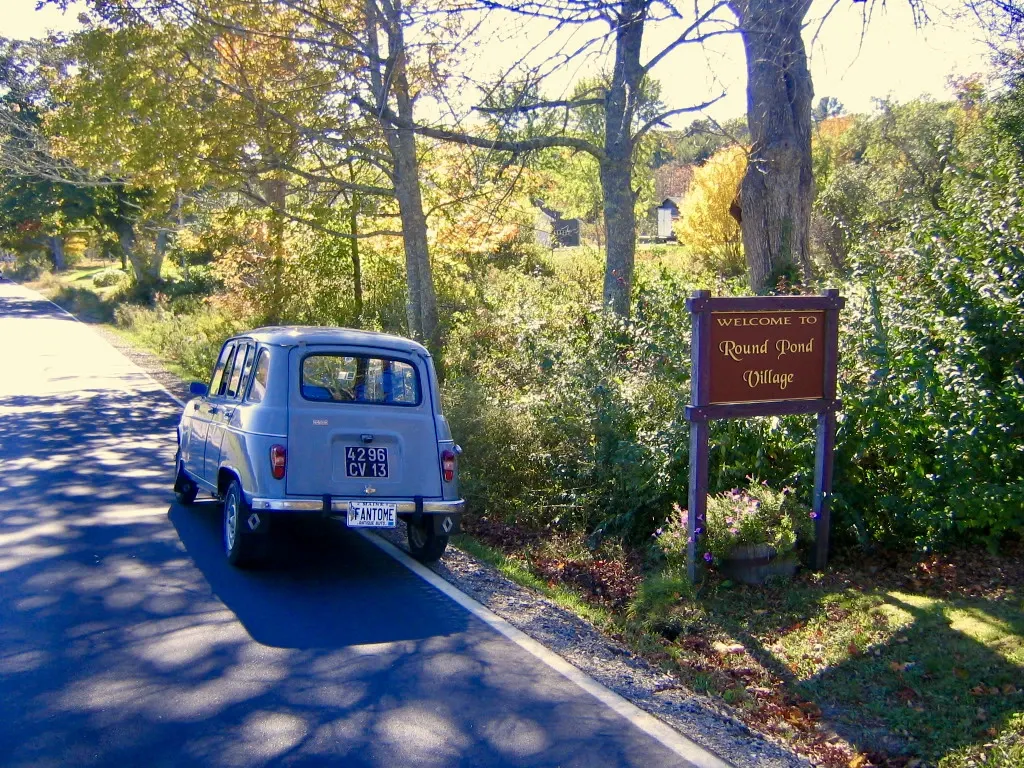 Vintage gray Renault 4L beside the Welcome to Round Pond Village sign in Maine