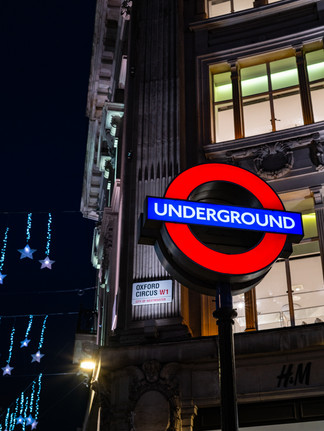 London Underground Sign Illuminated In the Dark With Christmas Lights In The Background.
