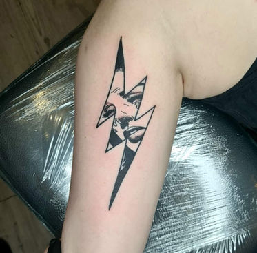 A lightning shaped tattoo with a womans face in distress in it. 
