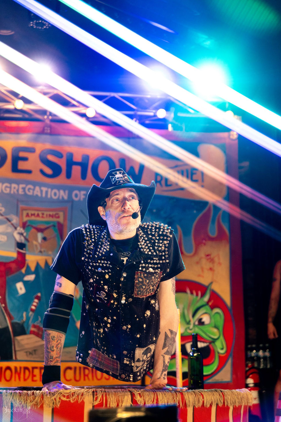 Ringmaster in a studded jacket and cowboy hat under laser beams