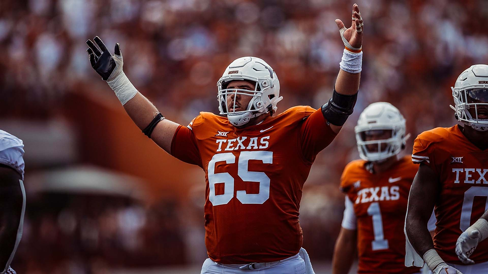 Football player in orange Texas jersey, number 65, raises arms in celebration on field. Blurred crowd in brown background.