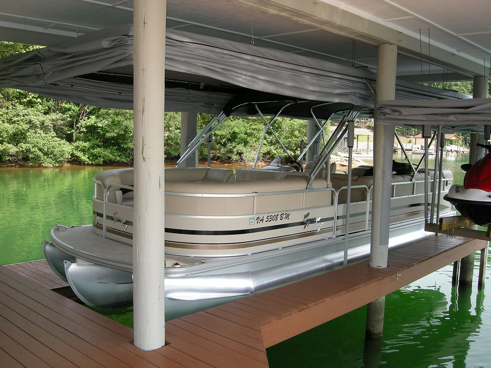 Pontoon boat docked under a covered boathouse with a wooden deck. Green water and lush trees are visible in the background.