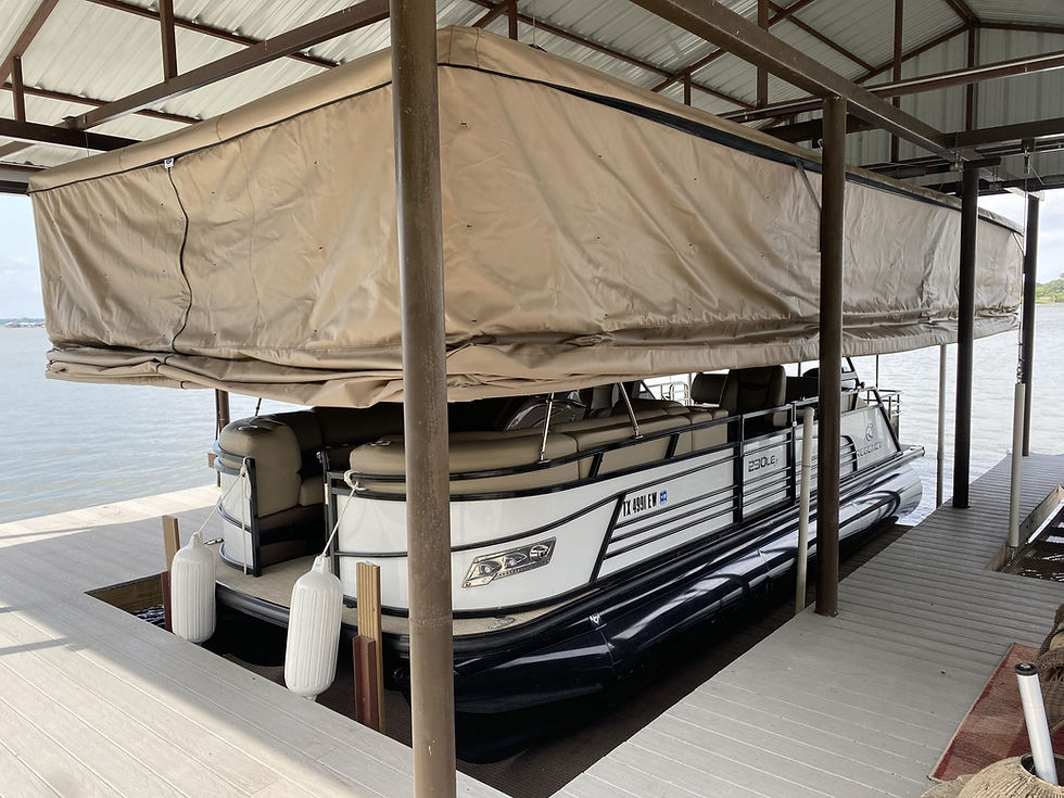 Pontoon boat stored under a dock roof with a raised cover system, open sides, seating, helm, and deck areas visible.