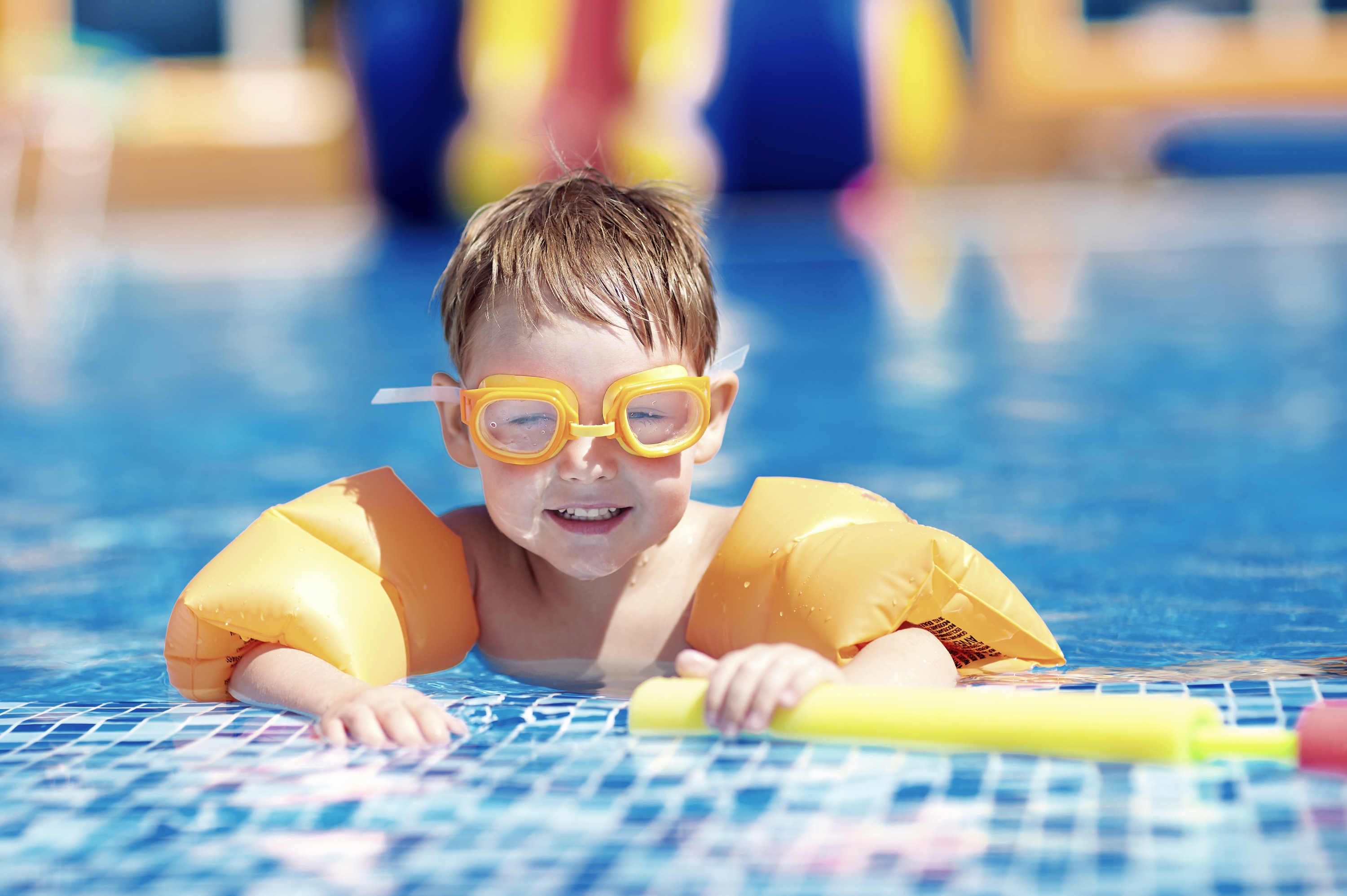 Ein kleiner Junge mit gelben Schwimmflügel und Taucherbrille im Pool.