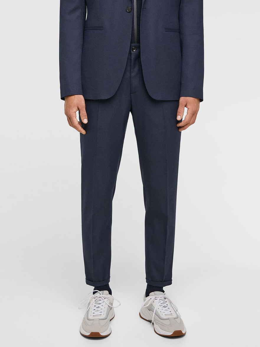 Man wearing a dark navy blue suit and white sneakers.