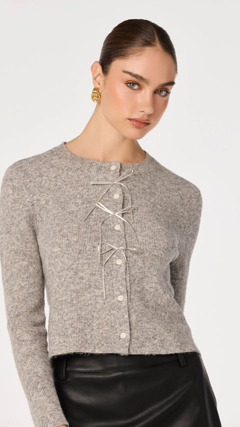 Woman wearing a grey cardigan with velvet bow ties.
