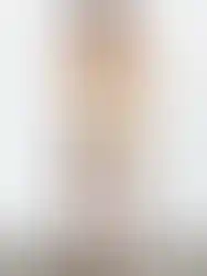 Woman wearing beige top with shorts; Carter Playsuit in studio background, facing away.