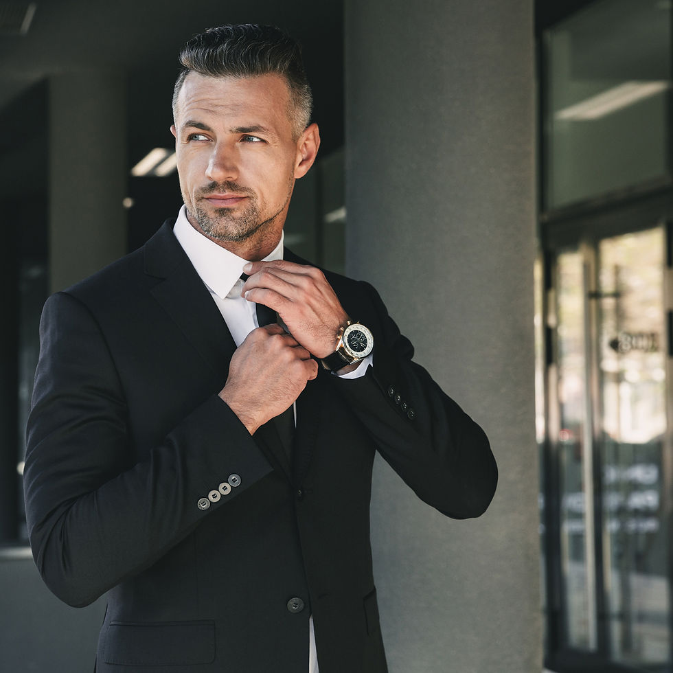 Well-dressed man adjusting tie, wearing a watch, standing near building entrance.