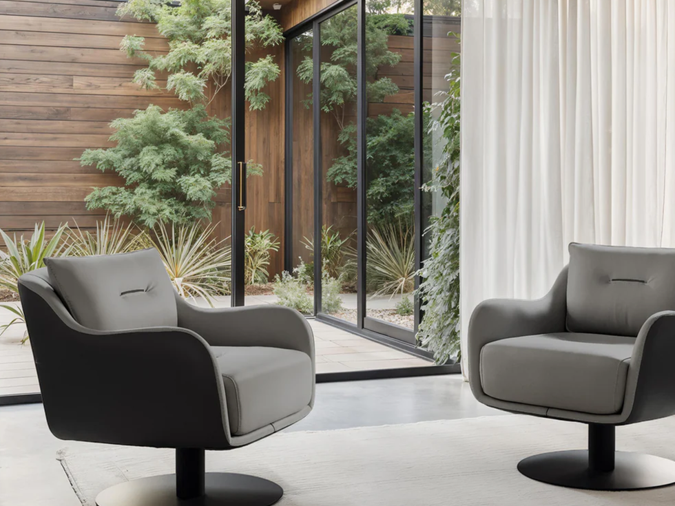 Two modern gray swivel chairs sit indoors near glass windows and drapes.