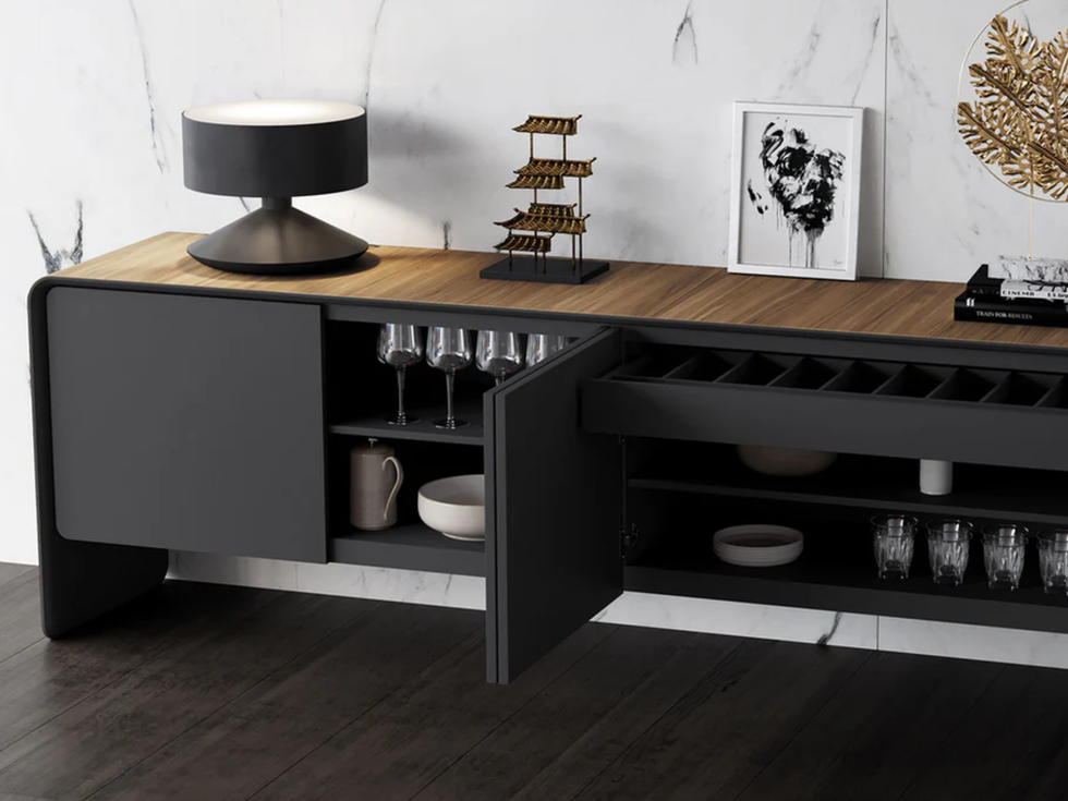 Modern sideboard with wine glasses, art, lamp, and decor against marble wall.