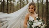 Bride in a forest with a flowing veil and bouquet.