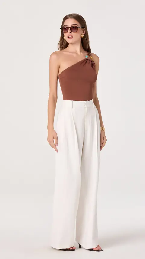 Woman wearing brown one-shoulder top and white trousers