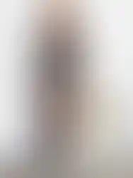 Woman wearing a black dress holding a hat, standing near white wall