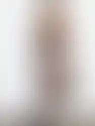 Woman wearing black top and floral skirt, standing in front of white wall.