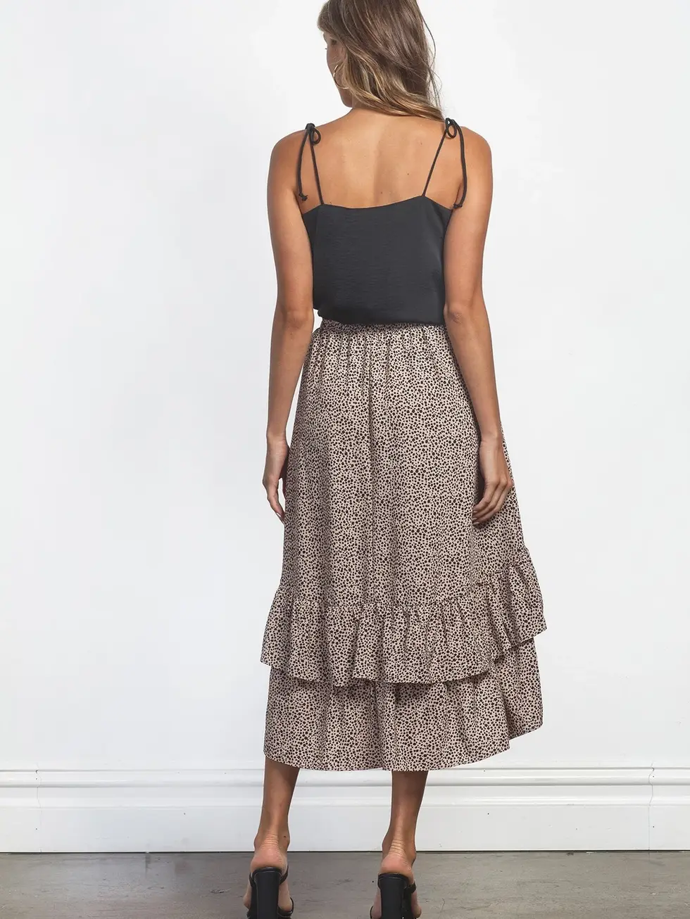 Woman wearing black top and floral skirt, standing in front of white wall.