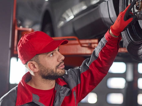 Mechanic in red uniform inspecting a car on a lift