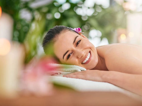 Smiling woman relaxing at a spa with candles and flowers.