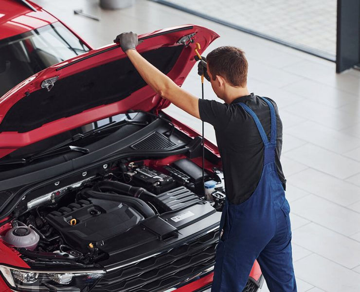 Mechanic in blue overalls inspecting a red car engine