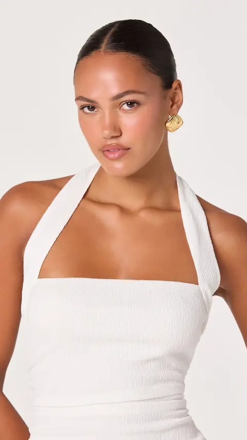Woman wearing a white halter top with gold earrings.
