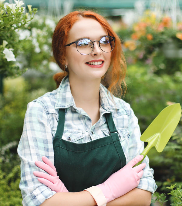 Smiling gardener with glasses, apron, holding trowel