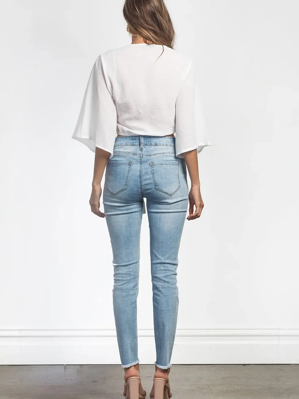 Woman wearing white top and denim jeans, standing, light background. Charme