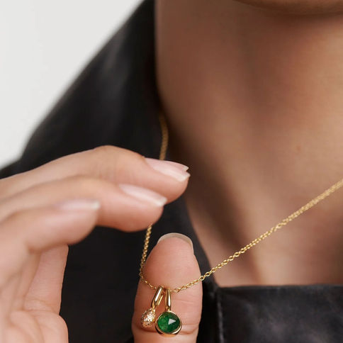 Woman displays delicate gold necklace with green and white gemstones