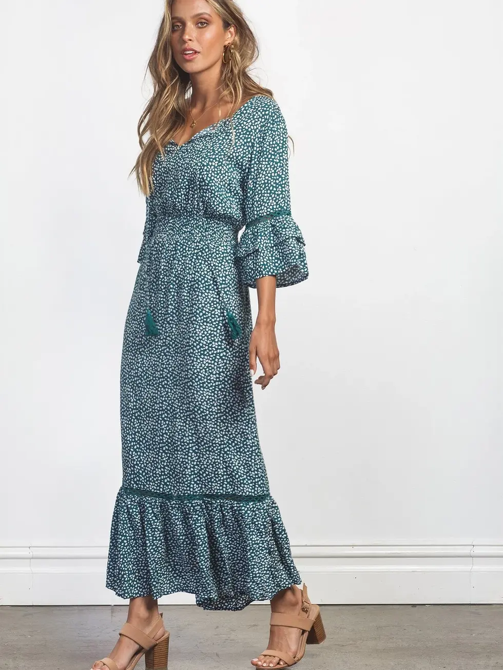 Woman wearing a blue floral dress posing by a white background. Charme.