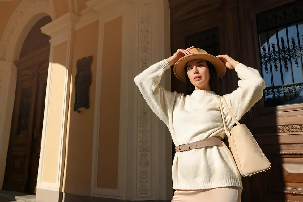 Woman wearing hat and holding it, beige outfit in front of building