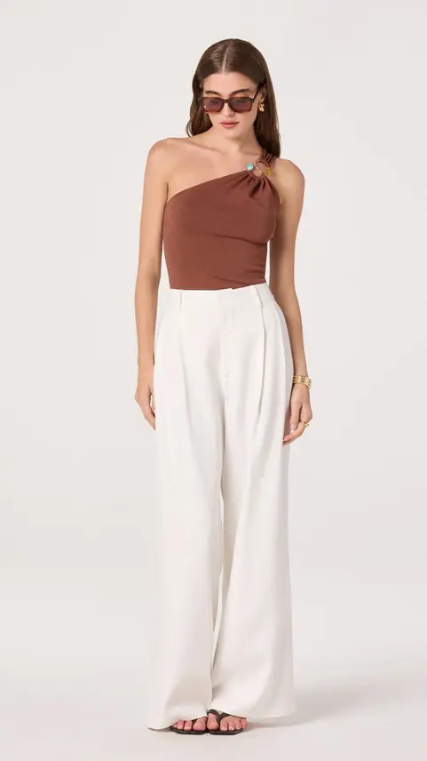 Woman wearing brown one-shoulder top and white trousers.