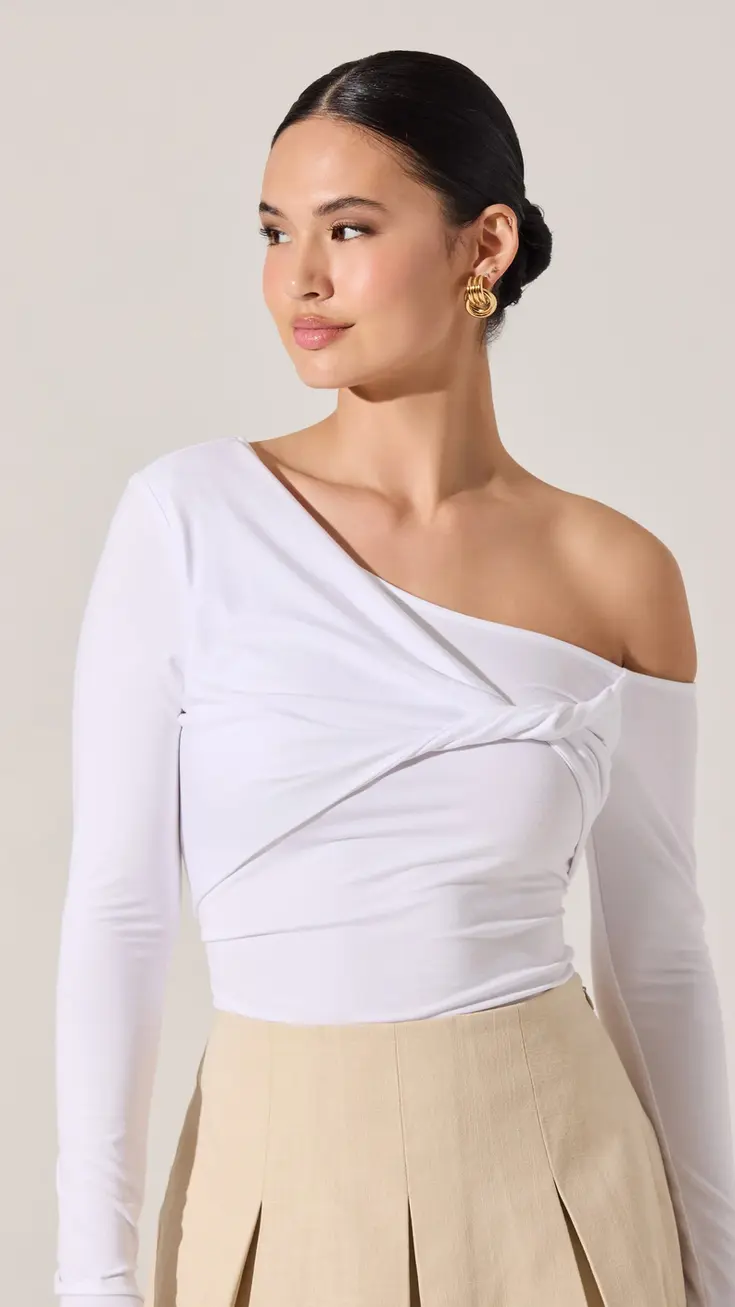 Woman wearing a white long-sleeve top with a knot detail and beige pleated skirt
