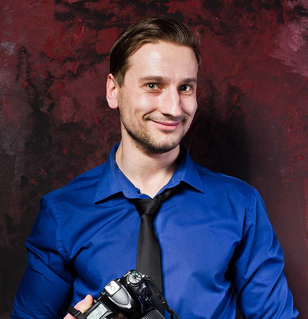 Smiling male photographer in a blue shirt holding a camera.