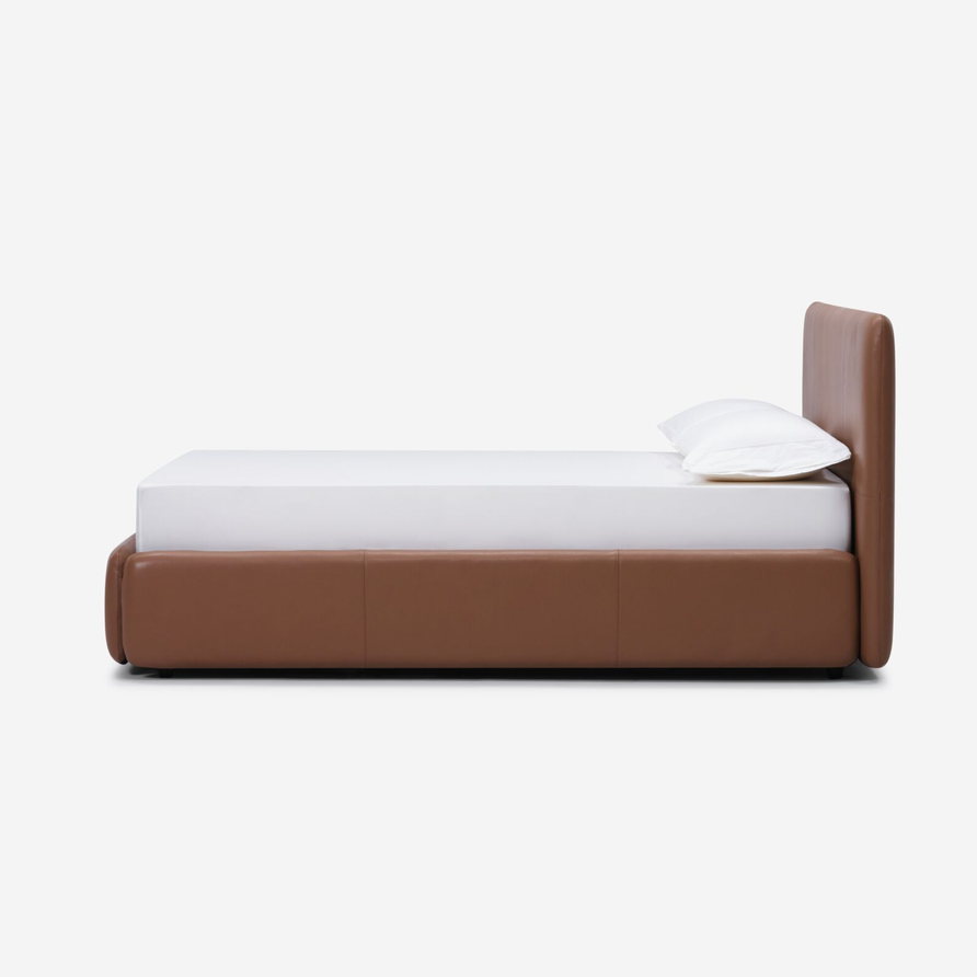 Brown leather bed frame with a white mattress and pillow