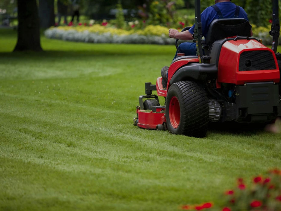 Person on red riding mower cutting a striped green lawn