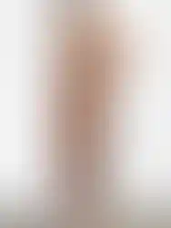 Woman wearing brown dress, sunglasses and sandals, standing by white wall.