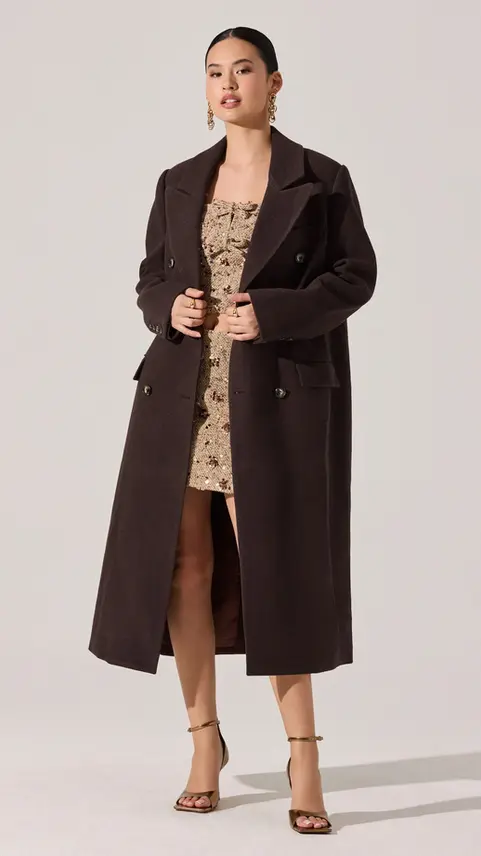 Model wearing a long black coat over a patterned dress.