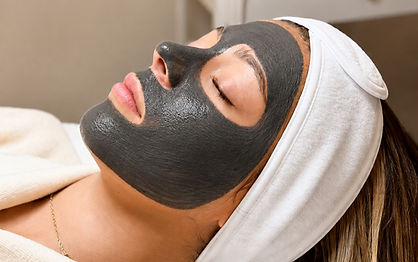 A relaxed guest with a charcoal face mask and a white headband during a facial
