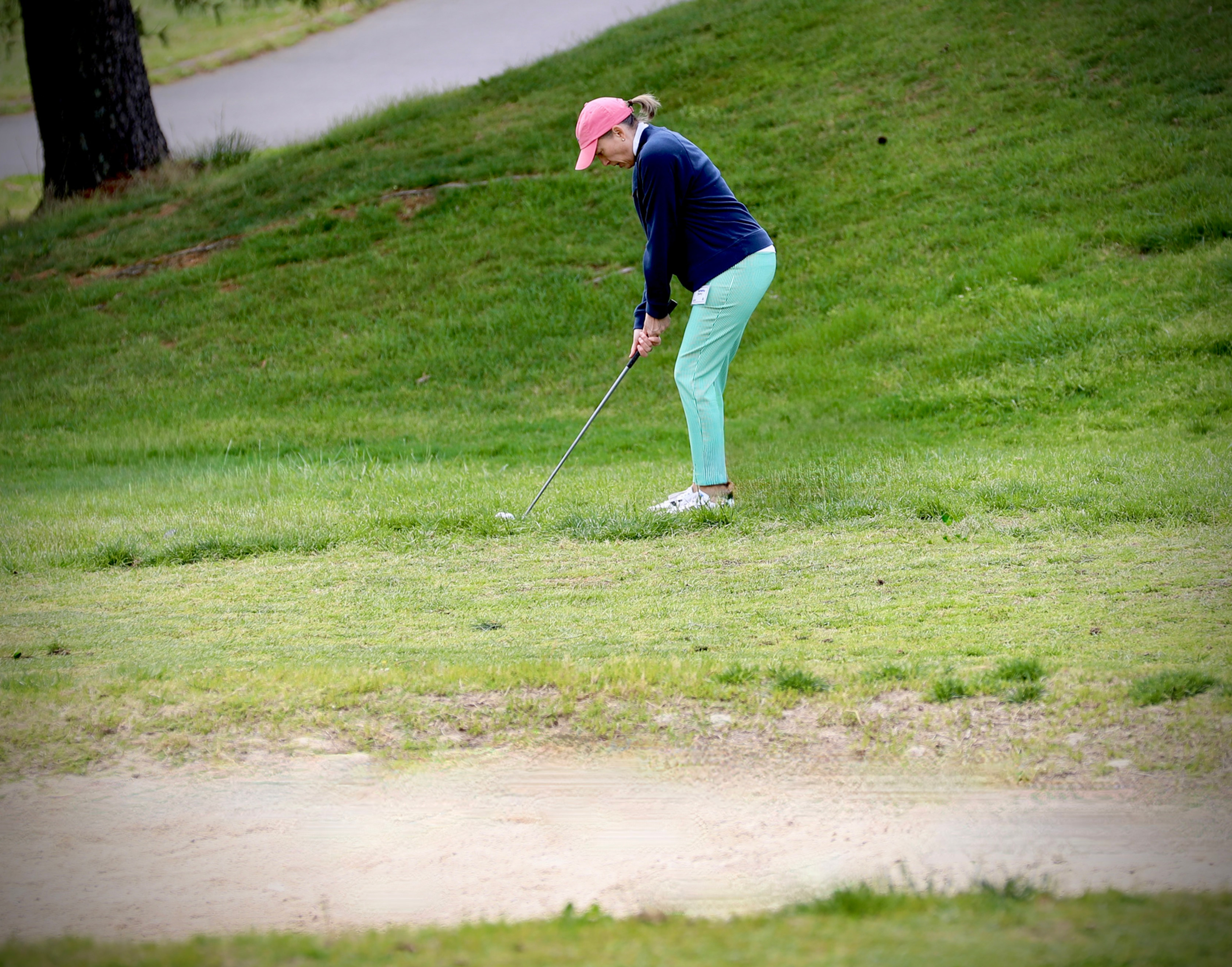 Golfer plays a shot from the grass near a bunker during a round of golf.