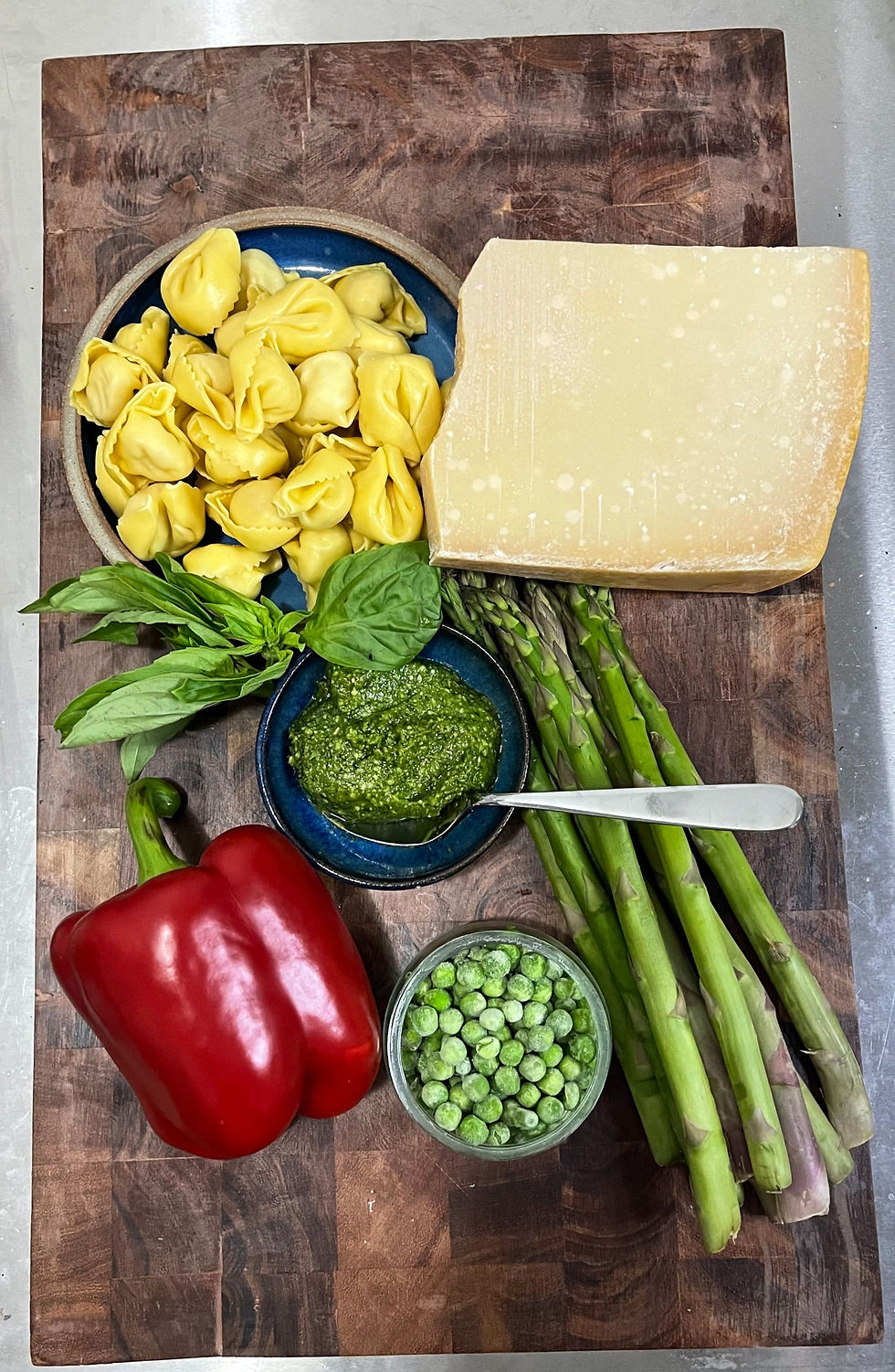 tortellini, vegetables, pesto, and cheese, on a brown board