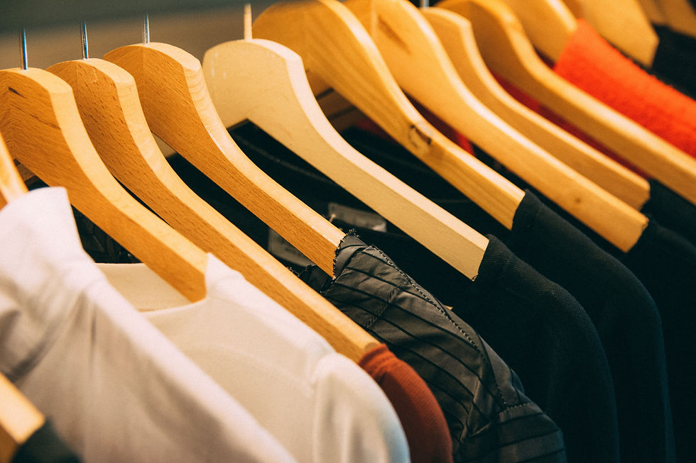 A close-up view of wooden hangers (with white, black and rustic orange coloured tops hanging from them) hanging from a clothing rail