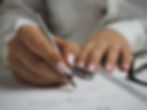 A woman with manicured nails, writing a clothing shopping list in a notebook