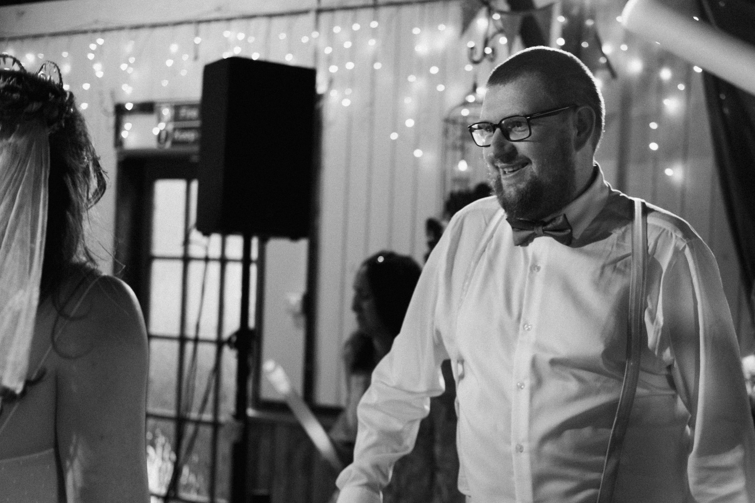 Black and white documentary wedding photograph of groom smiling during the evening reception