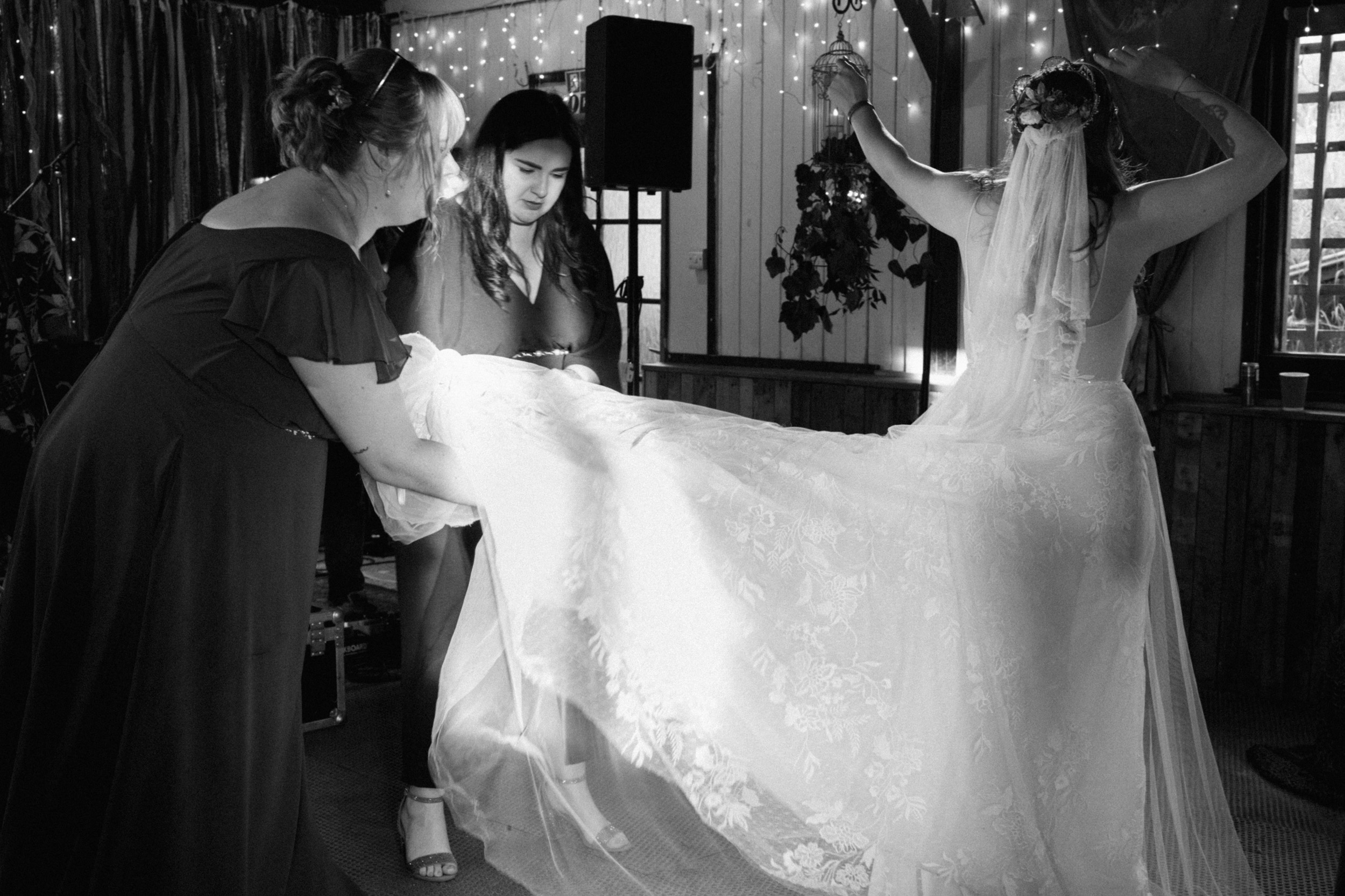 Bridesmaids lifting the bride's lace wedding dress on the dance floor during the reception.