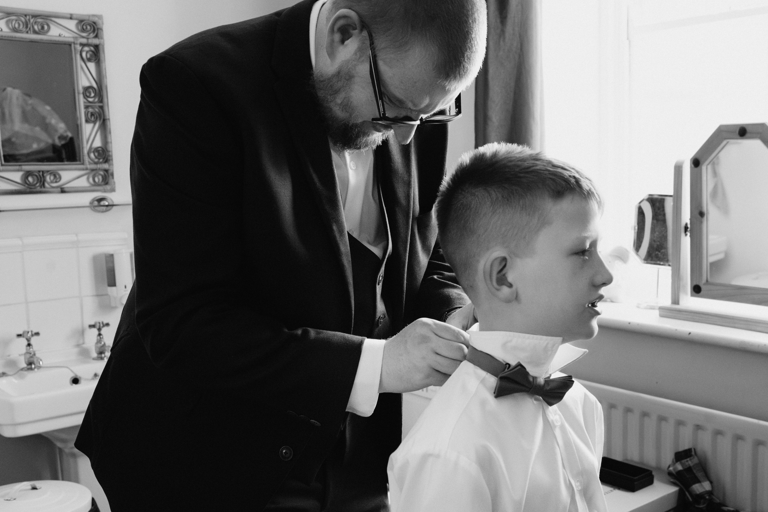 Documentary wedding photograph of groom helping a child get ready