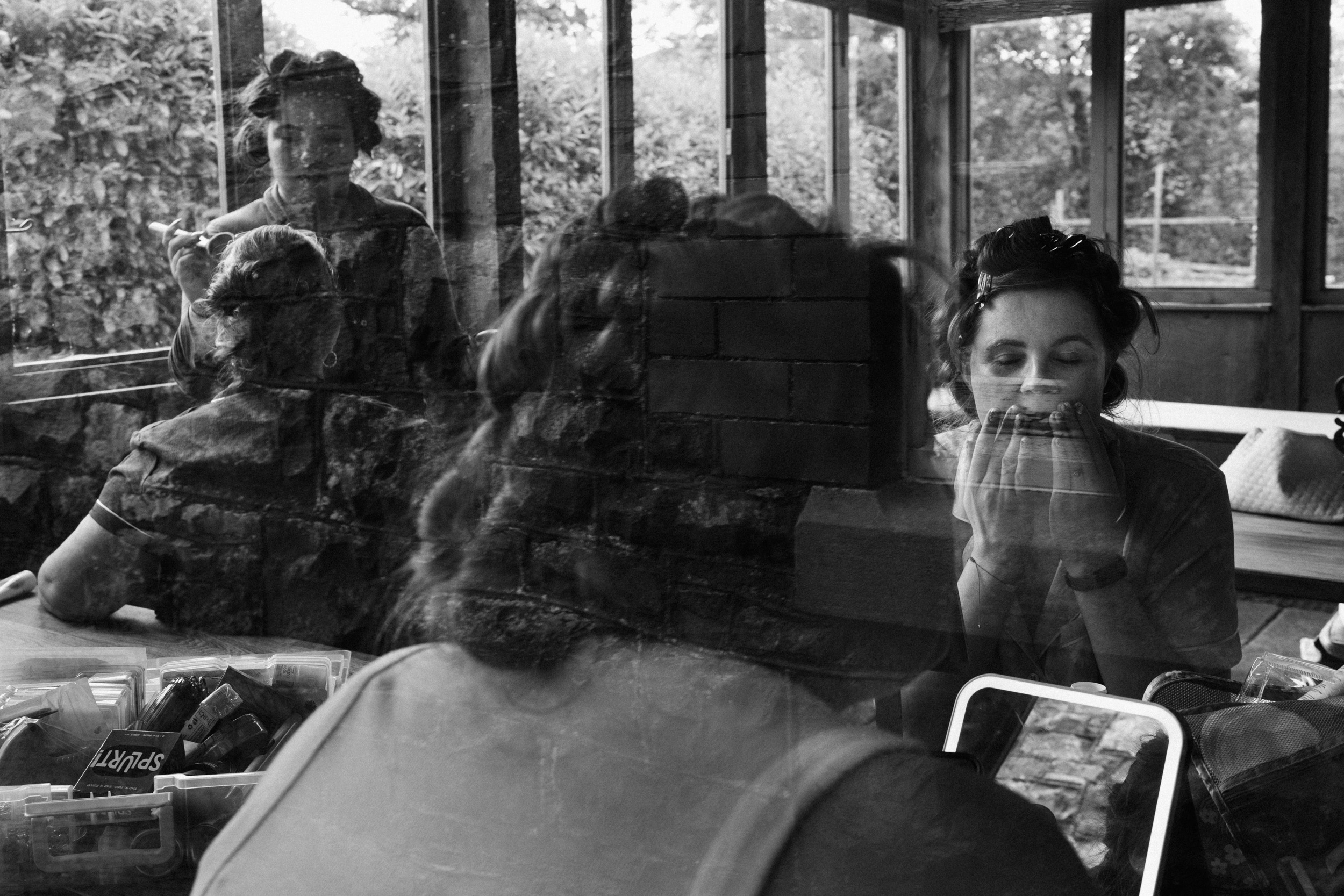 Black and white documentary wedding photograph of bridal preparations seen through glass
