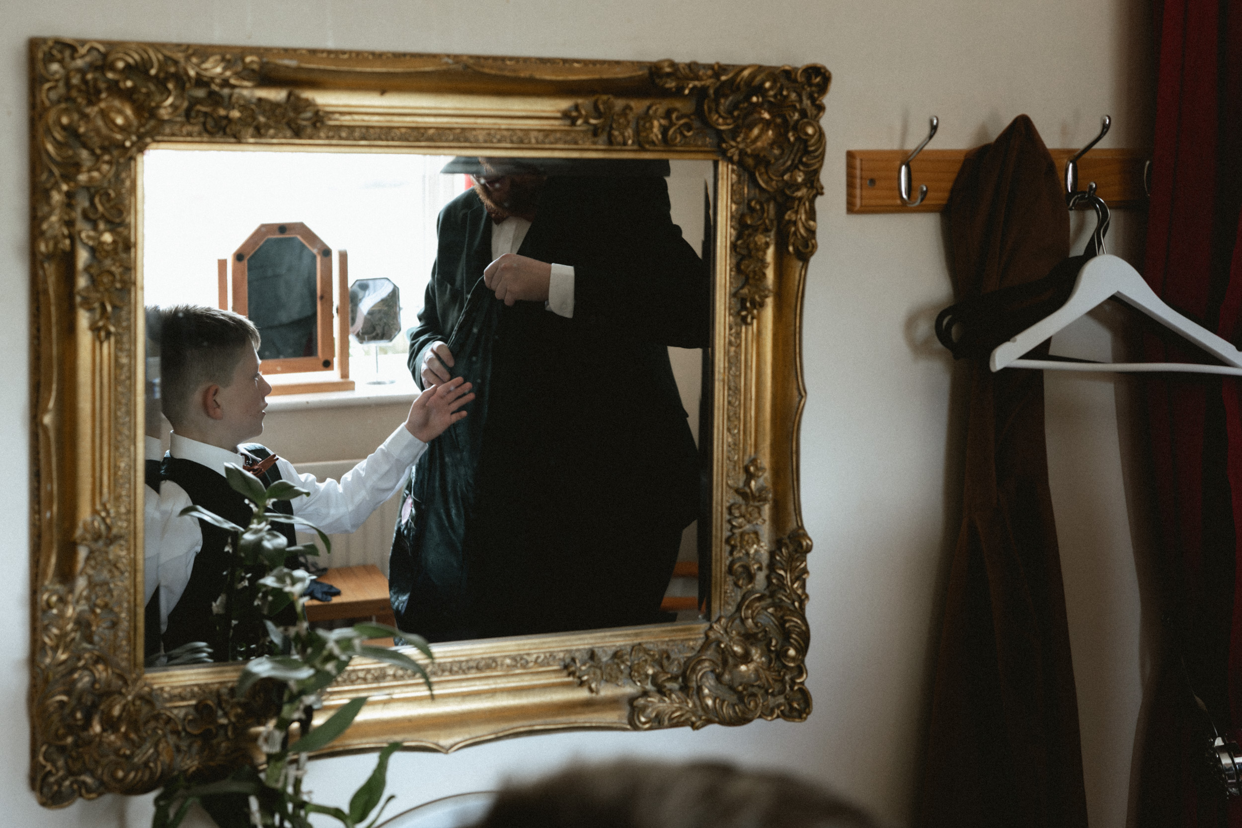 Documentary wedding photograph of a ring bearer putting on his jacket. 
