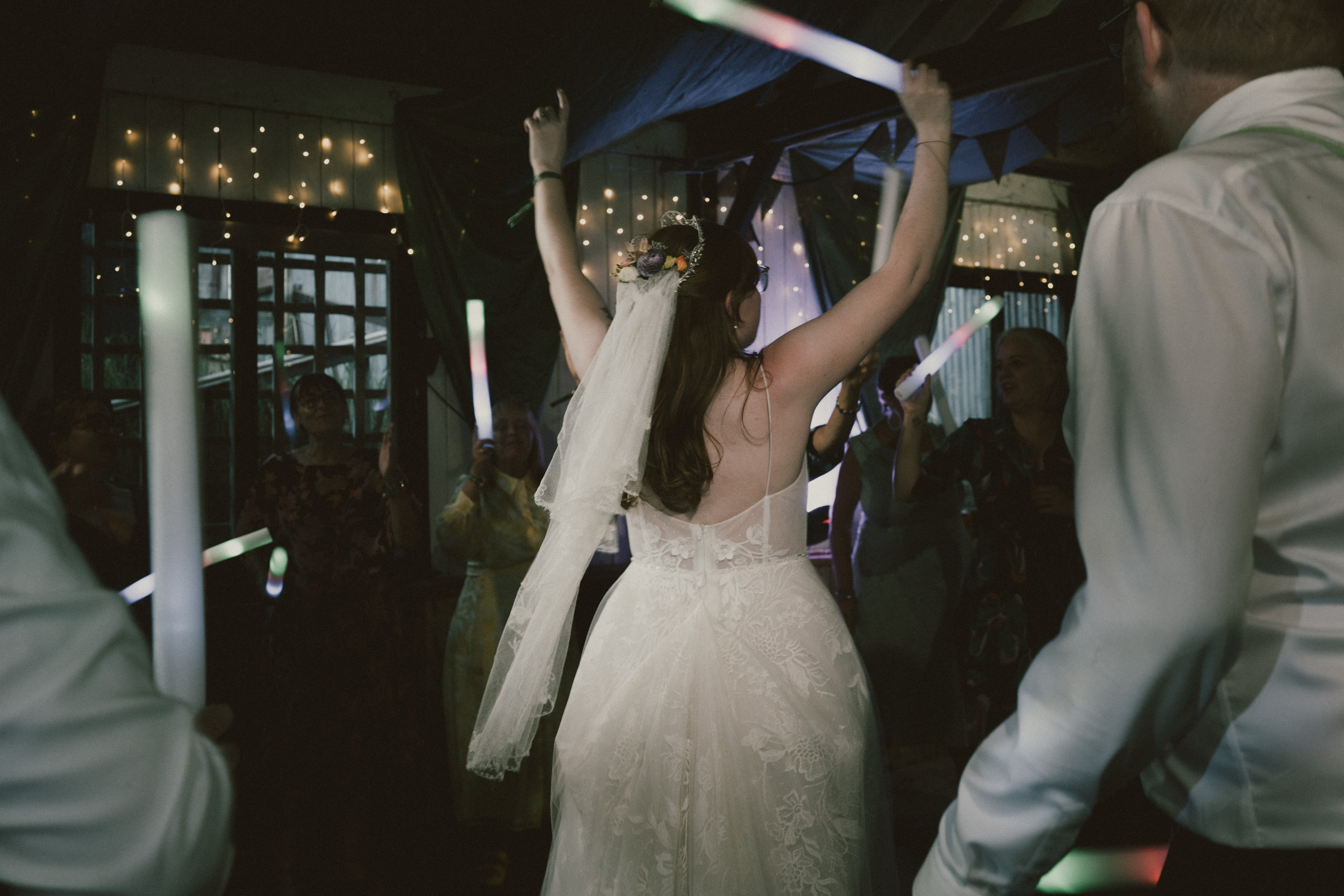 Colour documentary wedding photograph of bride dancing with guests and glow sticks