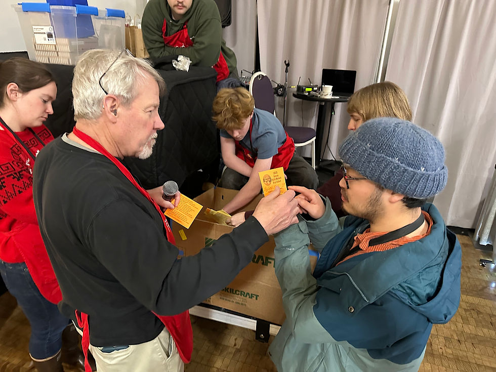 Juneau Public Market organizer Peter Metcalfe, left, and Fu Bao Hartle, a vendor selling his photographs at the market, conduct a prize drawing for shoppers at the Juneau Arts and Culture Center on Sunday, Nov. 30, 2025. (Mark Sabbatini / Juneau Independent)