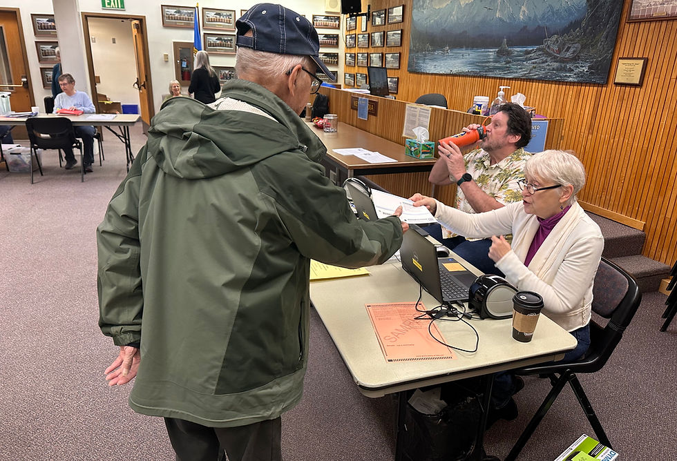 Larry Schutt receives his municipal election ballot from Jayne Andreen as she and Dave Lefbvre staff the entry table at the in-person voting center at City Hall on Tuesday, Oct. 6, 2026. (Mark Sabbatini / Juneau Independent)