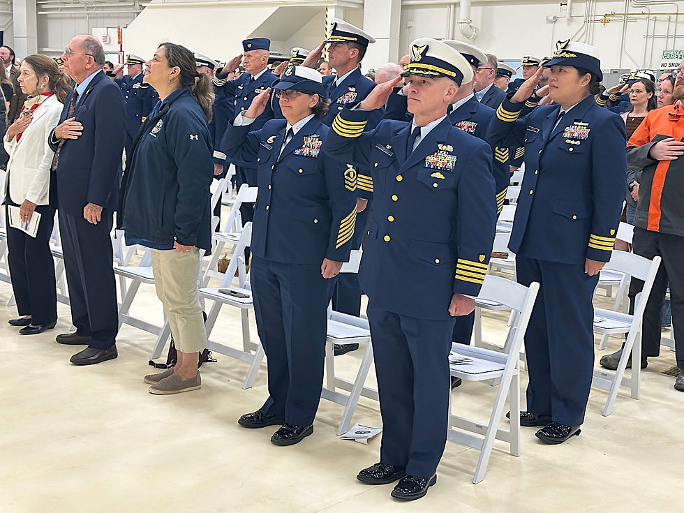 Attendees at a U.S. Coast Guard change of command ceremony stand for the national anthem at the Air National Guard Hangar in Juneau on July 11, 2025. (Mark Sabbatini / Juneau Independent)
