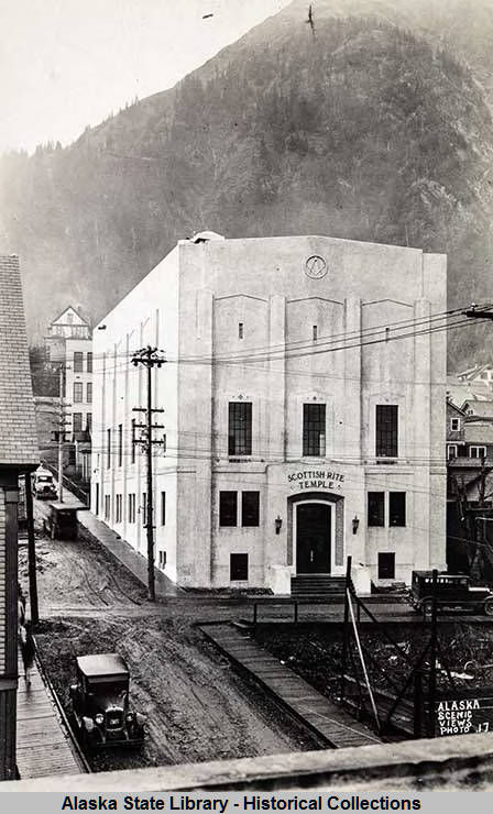 Scottish Rite Temple, located on Fourth Street and dedicated in 1928, is shown in this photo at that time. Note the muddy surface of Seward Street, not yet planked or paved. Neither the Capitol (1931) nor the Assembly Apartments (1932) had been built yet, as attested by the vacant lots now occupied by those structures. In 2009, the building was renamed Thomas B. Stewart Legislative Office Building. (Alaska State Library Historical Collections ASL-P103-013)